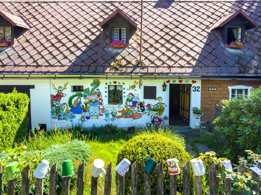 A small house with a painted wall and flowers in the front yard.